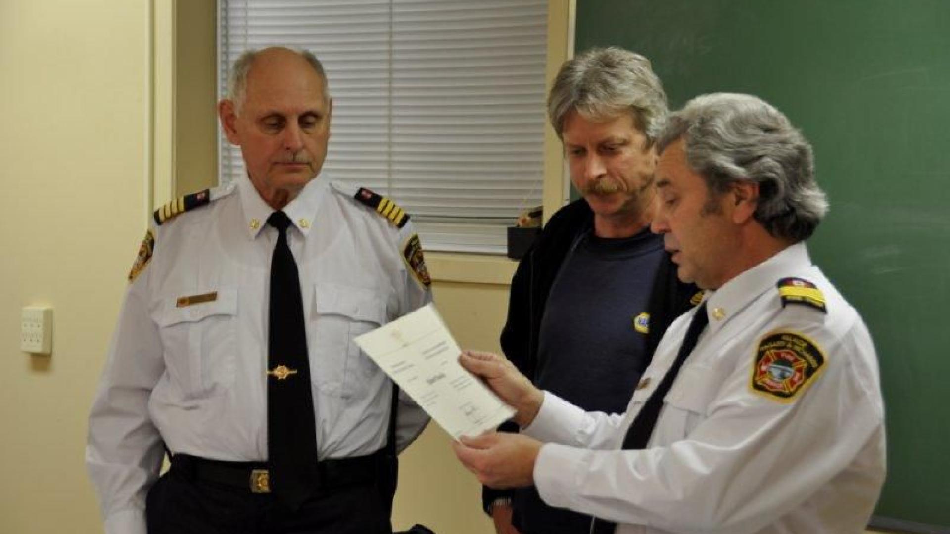 Three men in fire department uniforms, one holding a certificate.