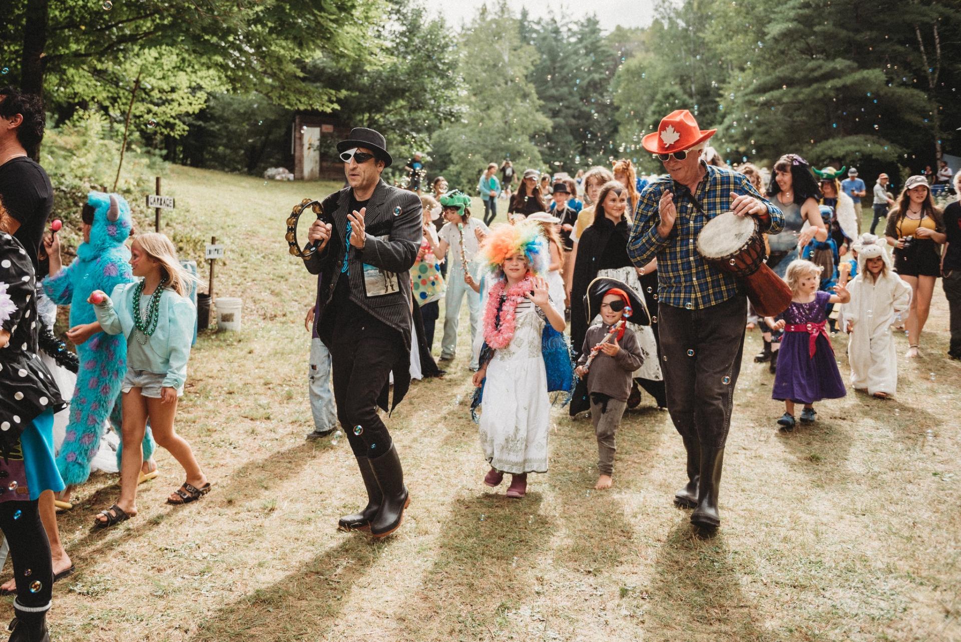parade of adults and children dressed up in costumes playing instruments in a large group